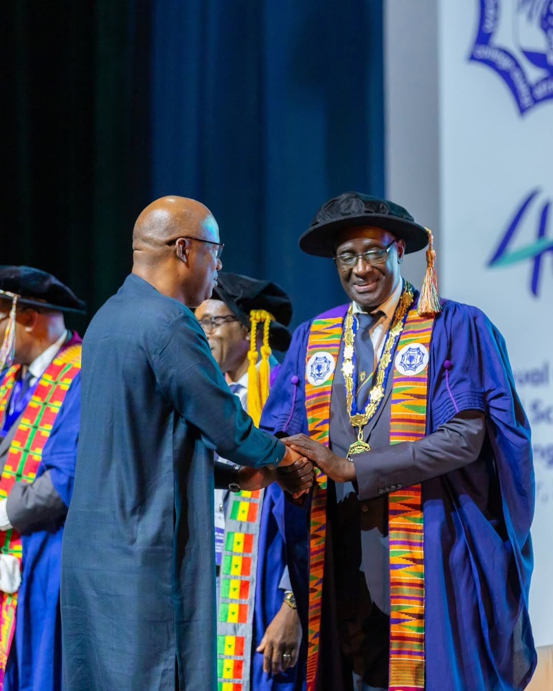 A Fellow in academic regalia greeting a delegate